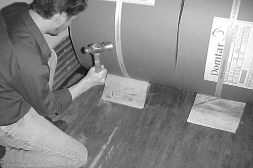 Picture of person hammering in a wedge under the tied down paper rolls