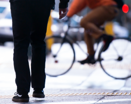Pedestrian standing on curb with bicyclist going by in background